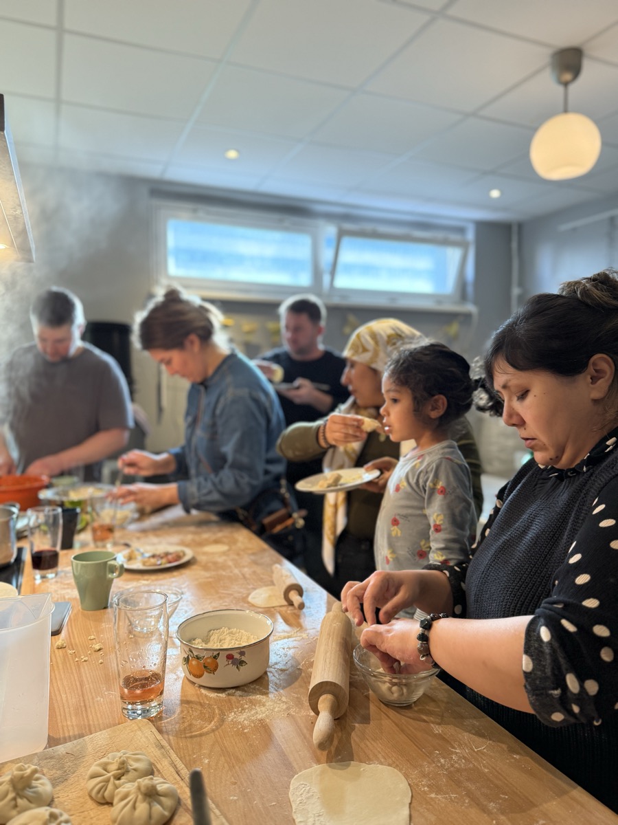 Nachbar*innen kochen gemeinsam Teigtaschen an einem langen Holztisch