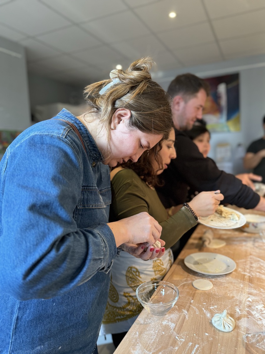 Mehrere Personen formen gemeinsam Teigtaschen an einem Holztisch